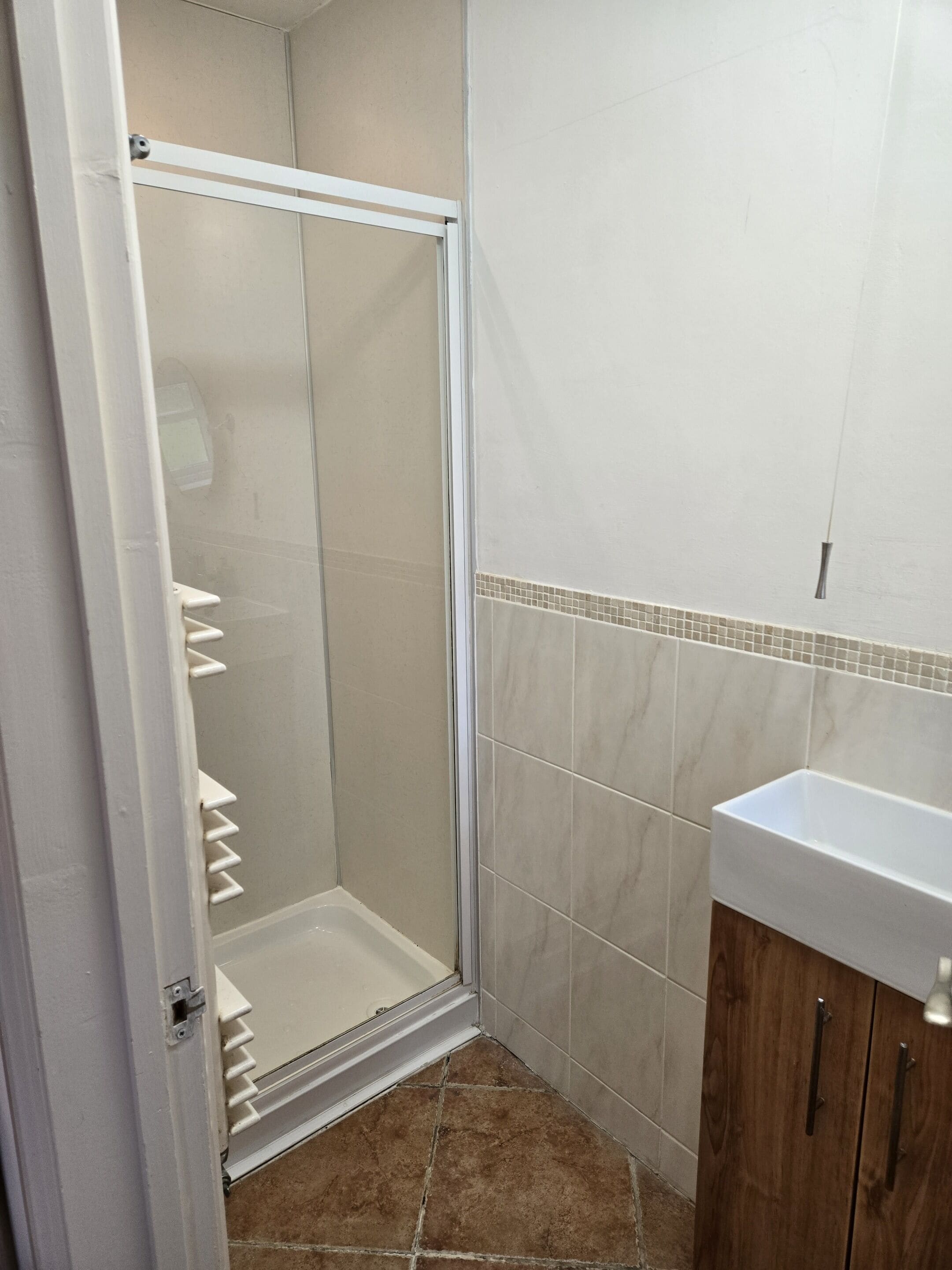 A bathroom with a shower, tiled walls, a sink, and wooden cabinets.