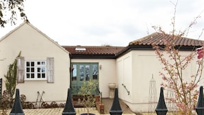 A building with a tiled roof, a door, and a window. There are potted plants and a fence in the foreground. - Wayside (Norwich)