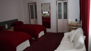 Et hotelværelse med to senge, en hvid sofa, et skrivebord og en stol.