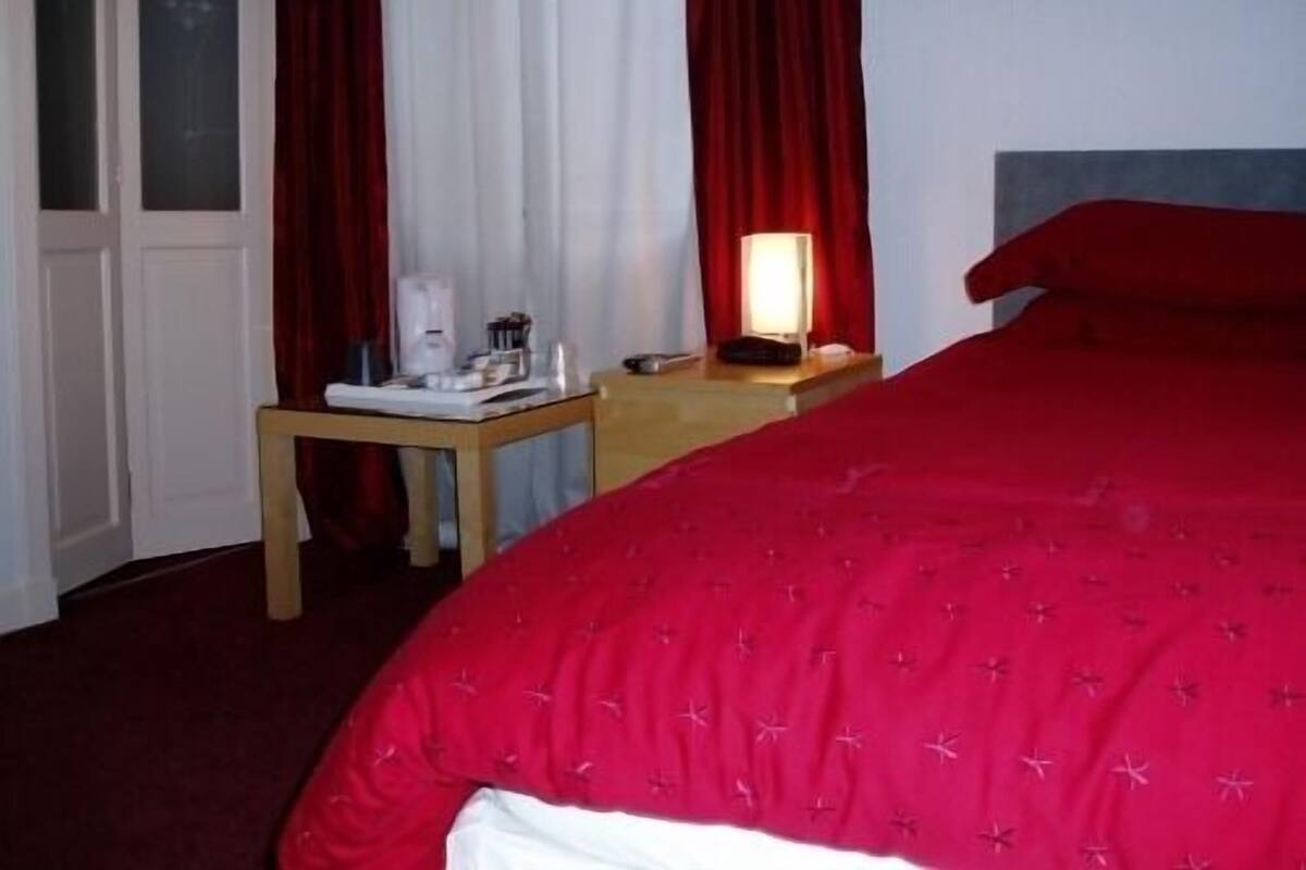 A hotel room with a bed, a nightstand, a lamp, and a coffee maker.