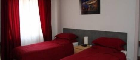 Une chambre d’hôtel avec deux lits simples, une literie rouge, une table de chevet et un tableau au mur.