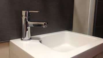 A modern bathroom with a chrome faucet and a white sink against a dark wall.