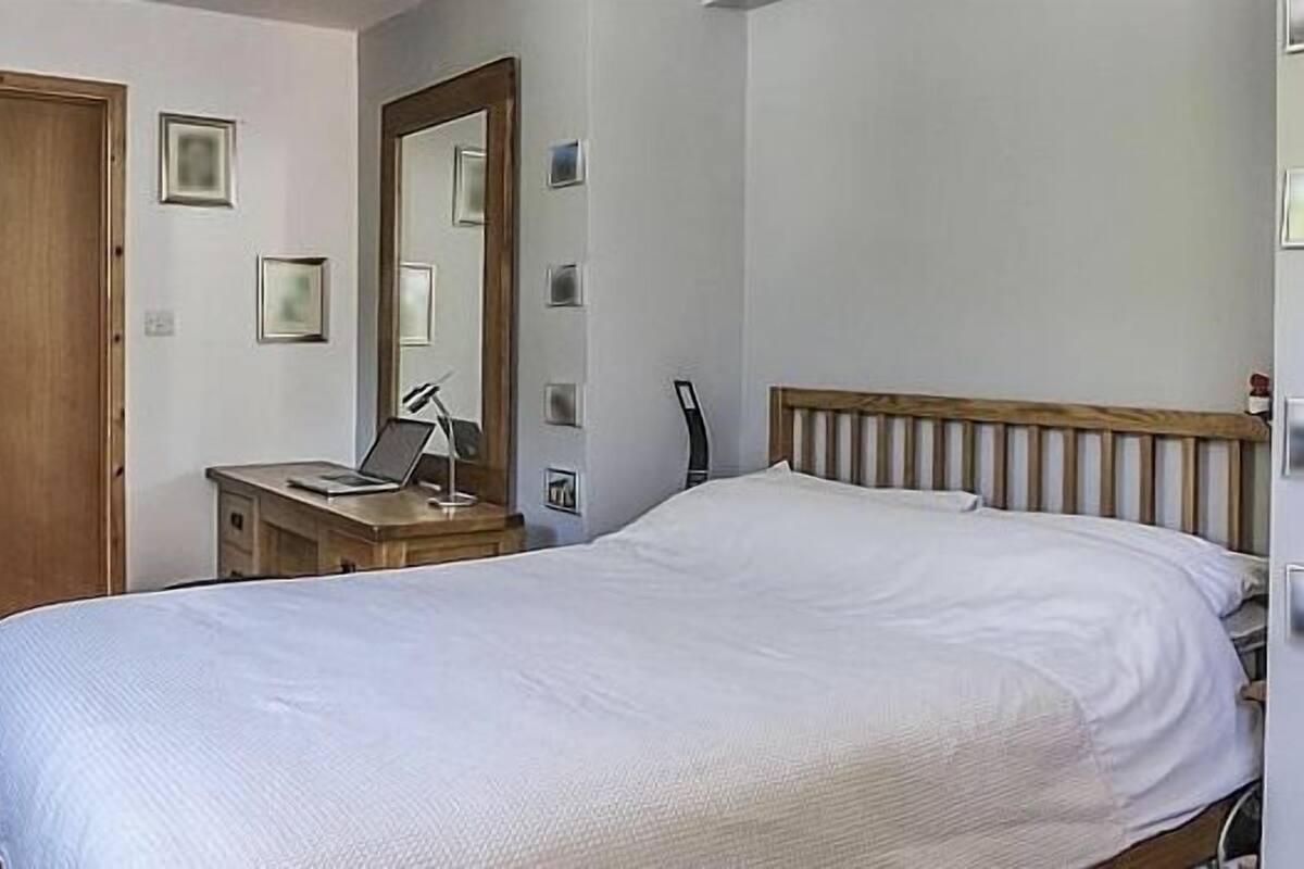A bedroom with a bed, a wooden desk with a chair, a mirror, and a door.