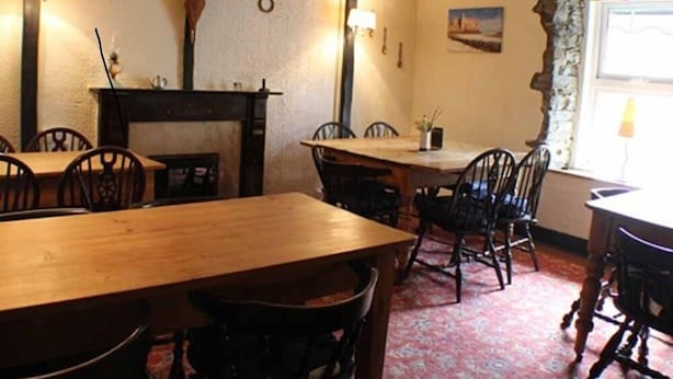 A dining area with wooden tables and chairs, a fireplace, and a window with curtains. - Afon Duad Inn (Carmarthen)