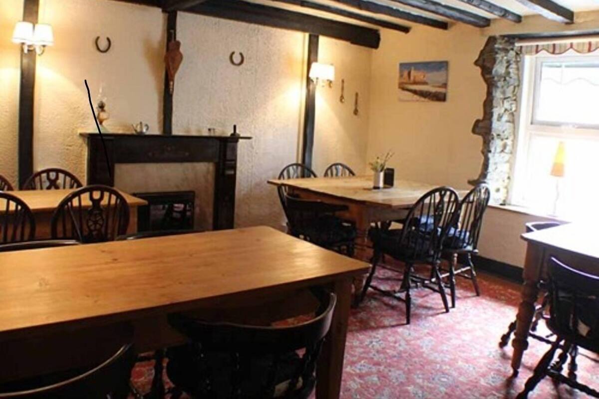 A dining area with wooden tables and chairs, a fireplace, and a window with curtains.