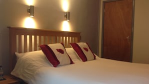 A neatly made bed with white bedding and two red pillows, a wooden headboard, and two wall-mounted light fixtures. - Afon Duad Inn (Carmarthen)