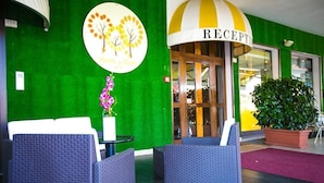 A hotel reception area with wicker furniture, a reception desk, and a large potted plant. - Hotel Agli Olmi (San Biagio di Callalta)