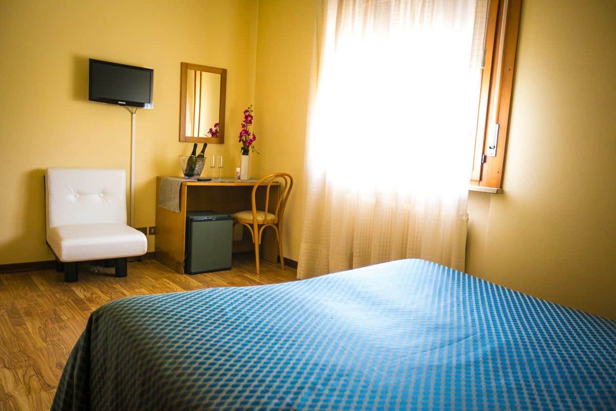 A hotel room with a bed, a desk, a chair, a television, and a window with curtains.