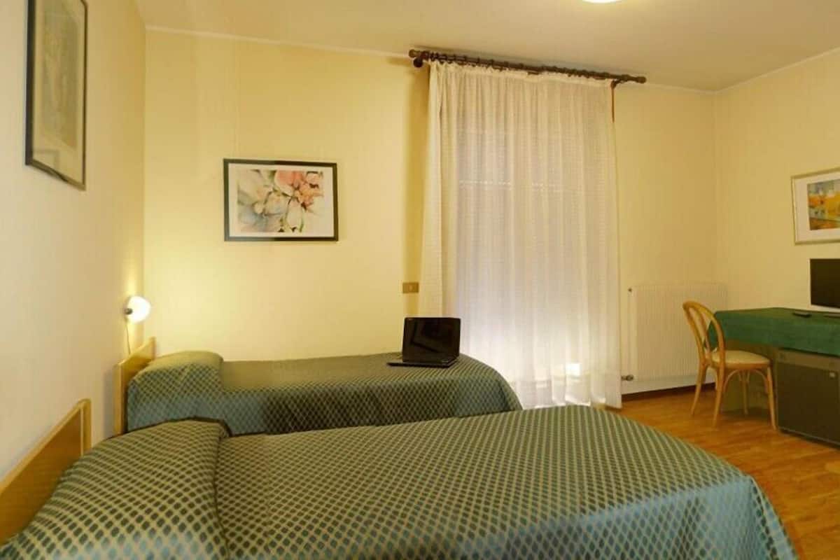 A room with two beds, a desk with a laptop, a chair, and a radiator.