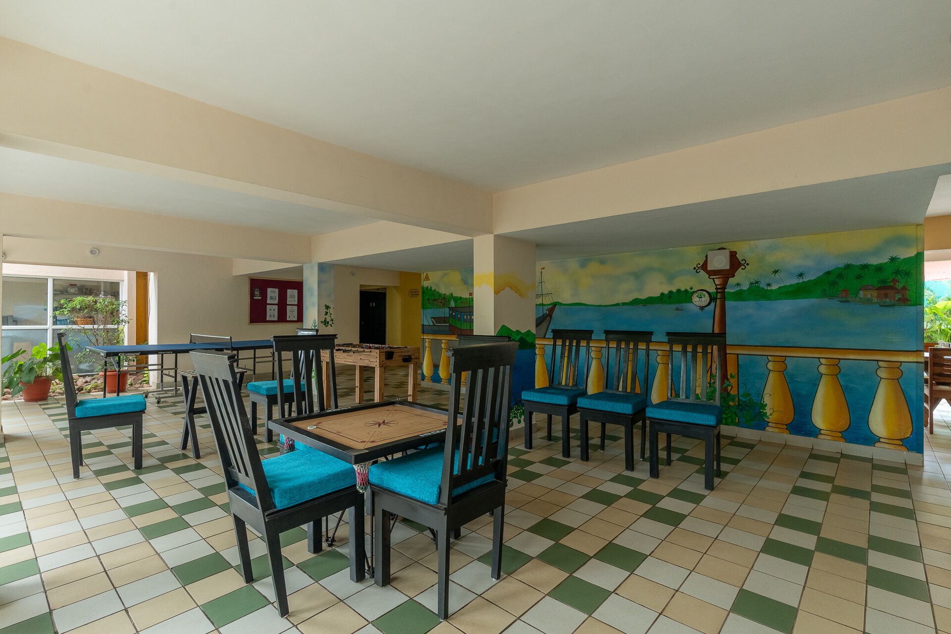 A spacious indoor area with a checkered floor, several wooden tables with chairs, and a mural depicting a coastal scene.