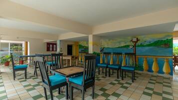 A spacious indoor area with a checkered floor, several wooden tables with chairs, and a mural depicting a coastal scene.