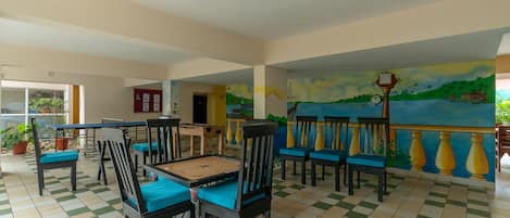 A spacious indoor area with a checkered floor, several wooden tables with chairs, and a mural depicting a coastal scene.
