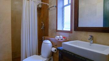 A bathroom with a toilet, shower, sink, and a window.