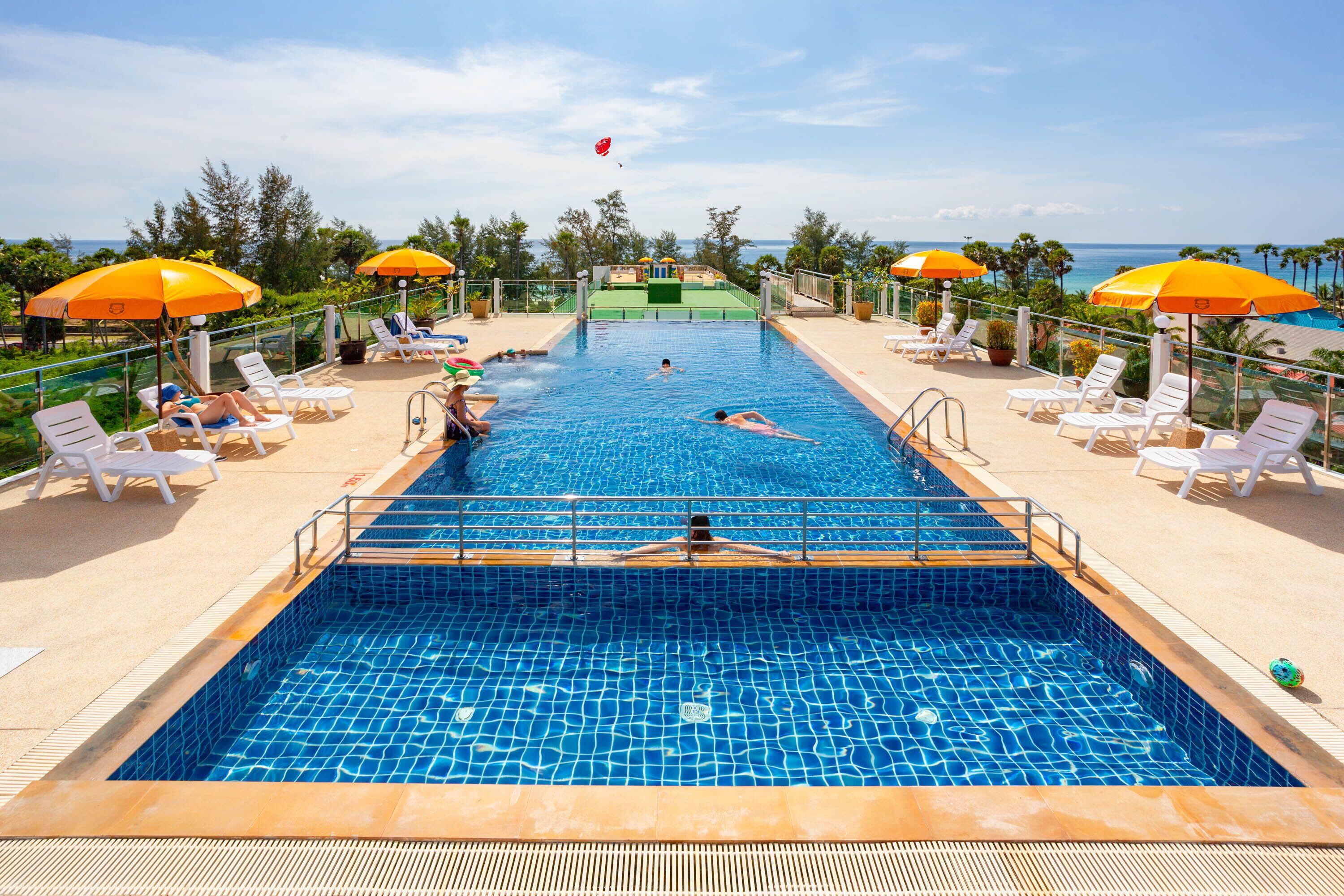 A swimming pool with lounge chairs and umbrellas, surrounded by trees and a view of the ocean.