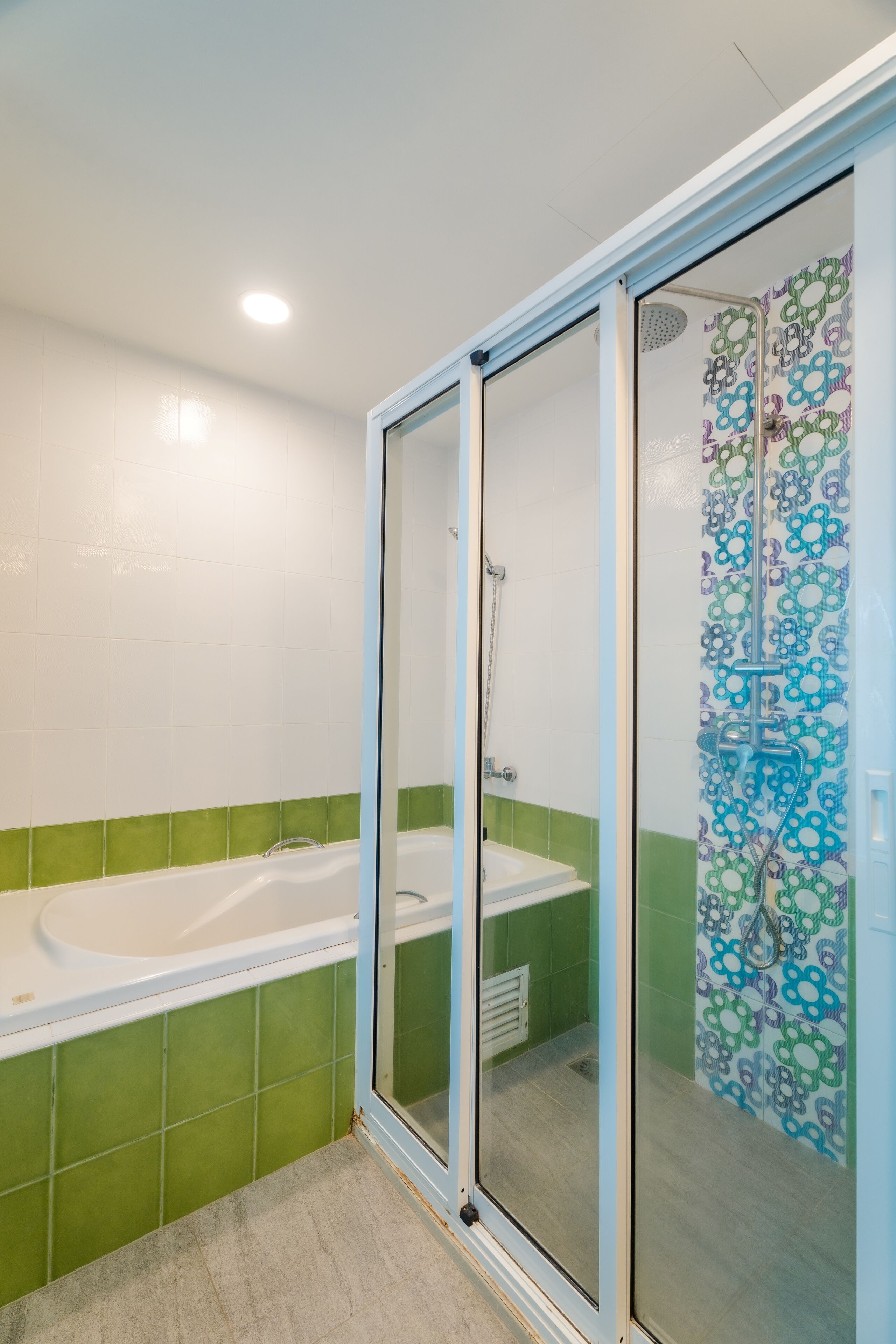 A bathroom with a glass-enclosed shower, a bathtub, and green-tiled walls.
