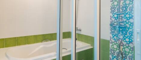 A bathroom with a glass-enclosed shower, a bathtub, and green-tiled walls.