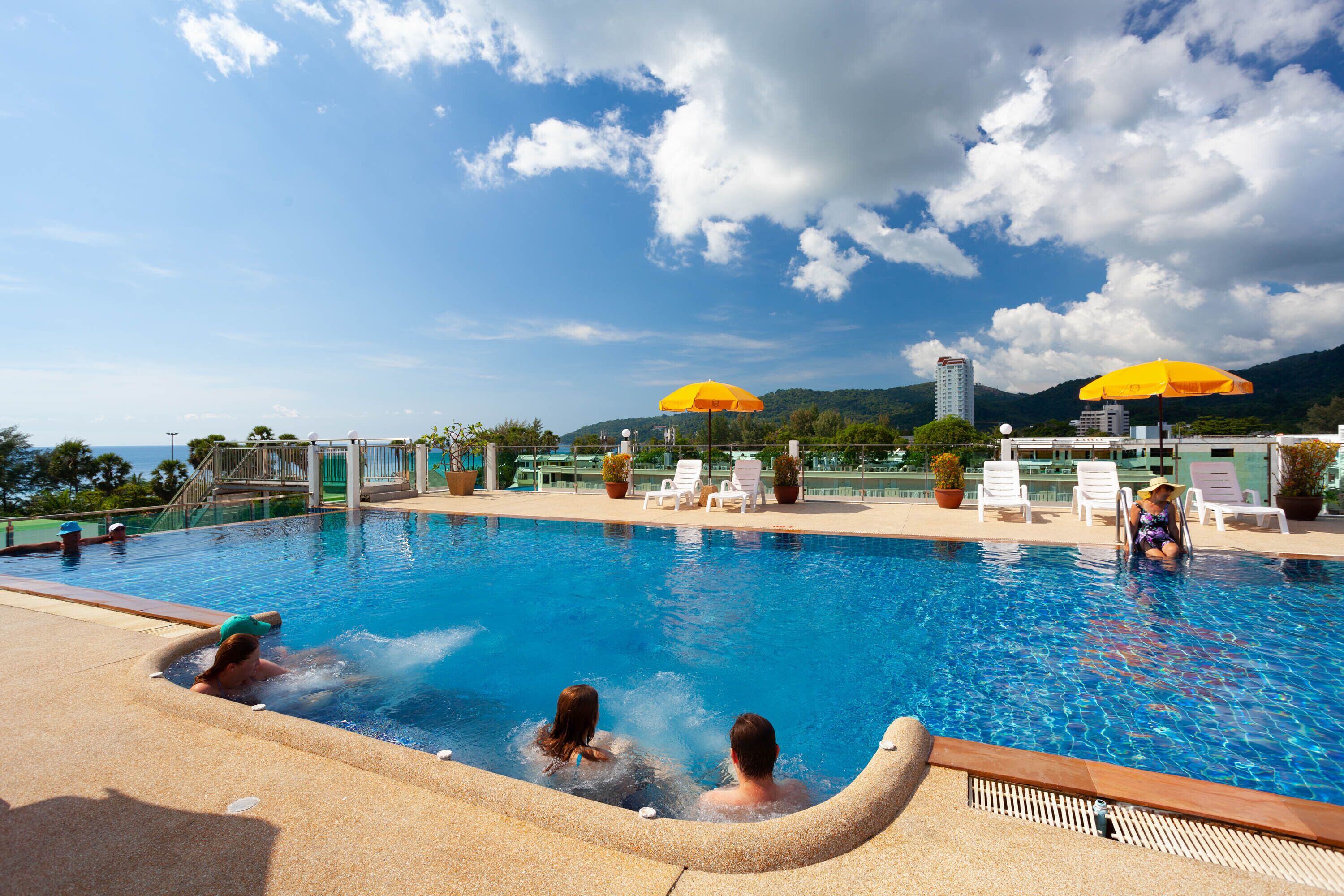 A swimming pool with lounge chairs and umbrellas, surrounded by greenery and a mountain in the background.