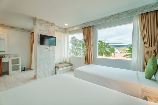 Habitación de hotel con una cama grande, televisión montada en la pared, escritorio y ventana con cortinas.