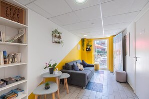 A modern room with a sofa, a small table, a bookshelf, and a potted plant.