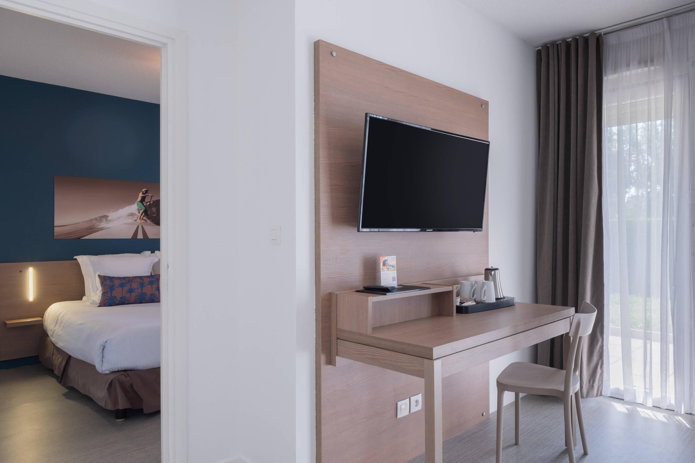 Ein Hotelzimmer mit Bett, Schreibtisch, Stuhl, Fernseher und einem fenster mit Vorhängen.