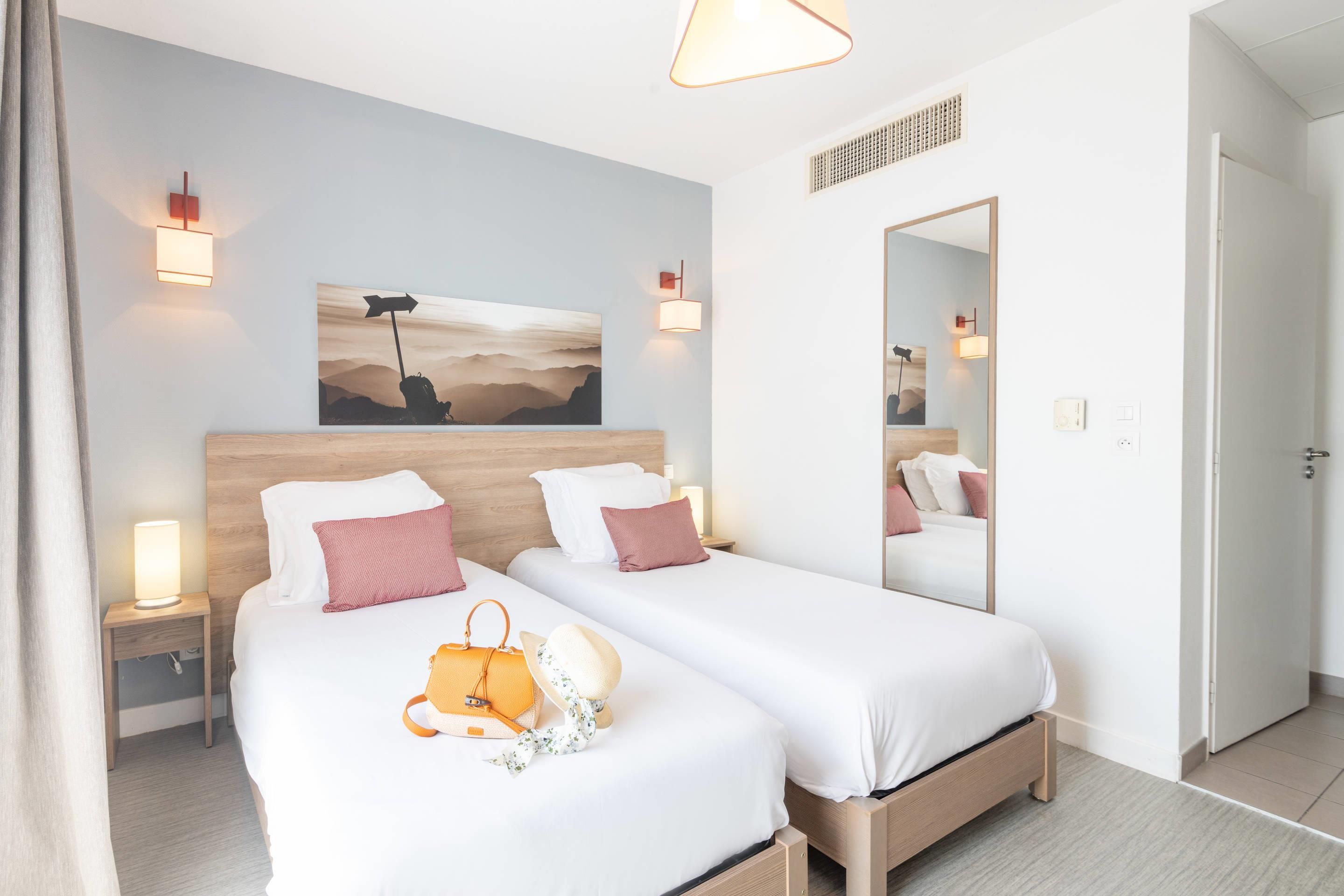 Habitació d'hotel amb dos llits, un mirall gran i obra d'art a la paret.