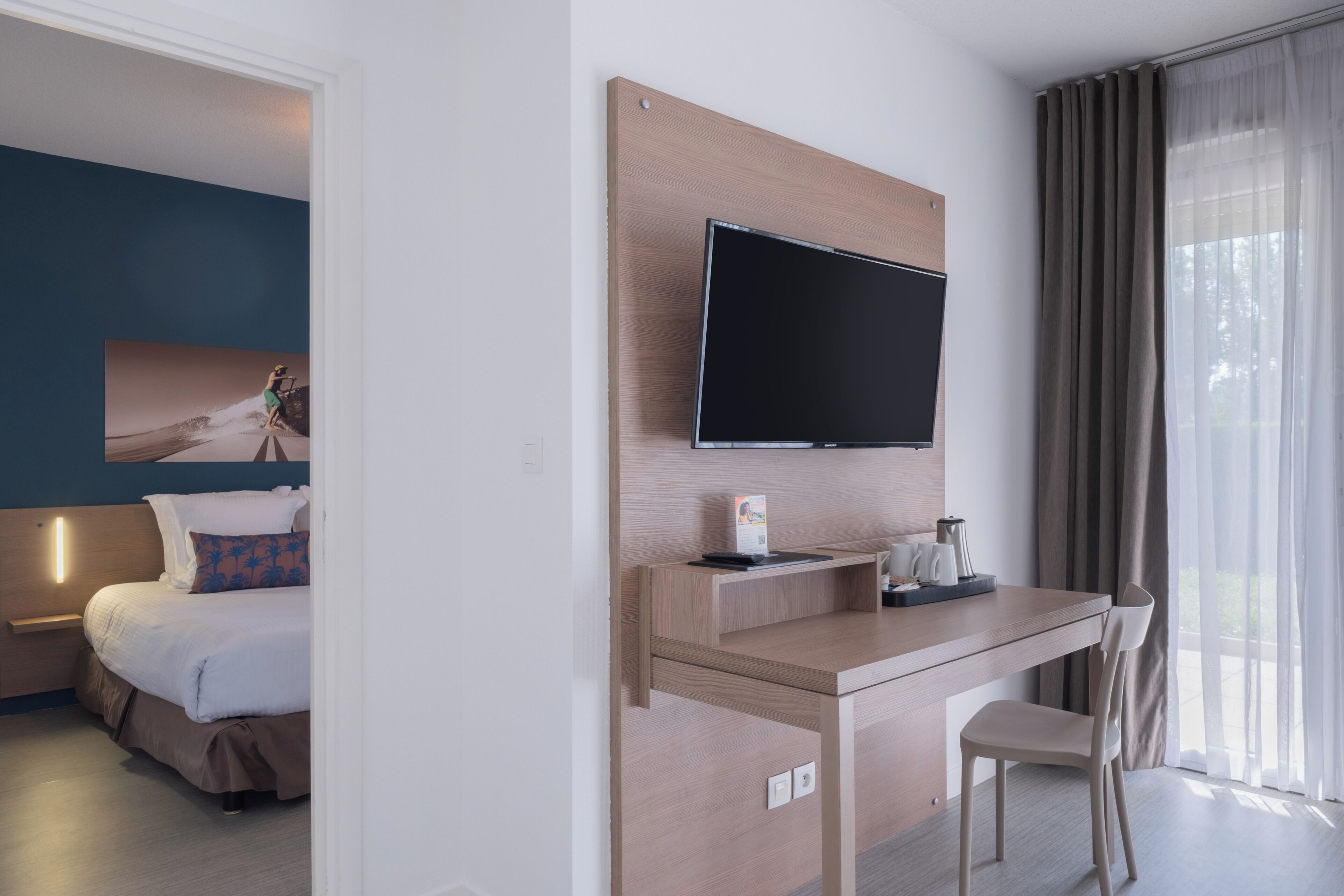A hotel room with a bed, a desk, a television, and a window with curtains.
