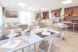 Un espace de restauration moderne dans un hôtel, avec plusieurs tables, des chaises et un coin cuisine en arrière-plan.