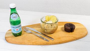 Una botella de agua Spellegrino, un cuenco de vidrio con un postre y un bombón de chocolate sobre una tabla de madera.