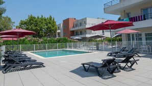 Un espace piscine avec des chaises longues et des parasols, entouré d’une clôture et de bâtiments.