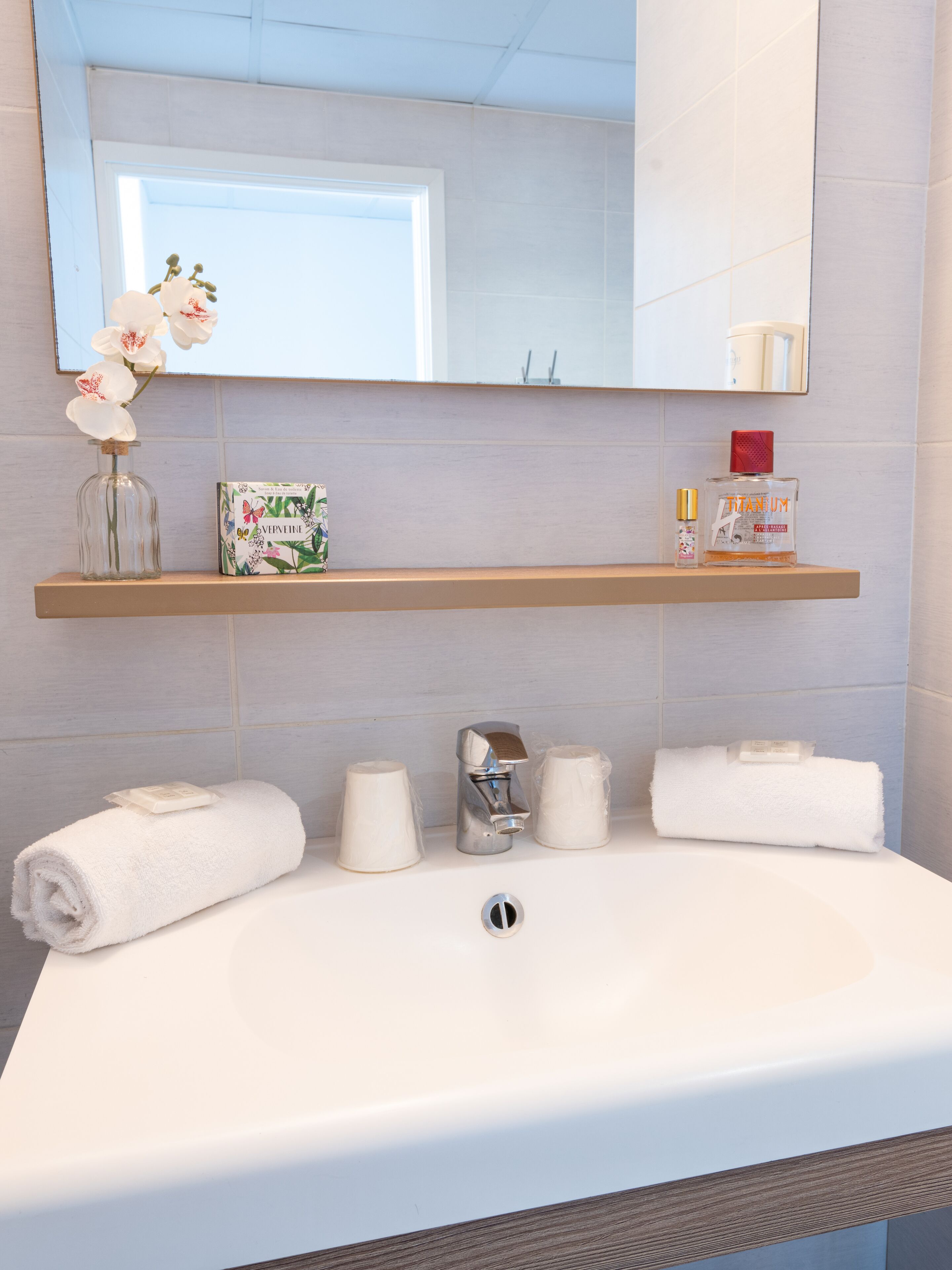 A bathroom with a white sink, a mirror above it, and a shelf with toiletries.