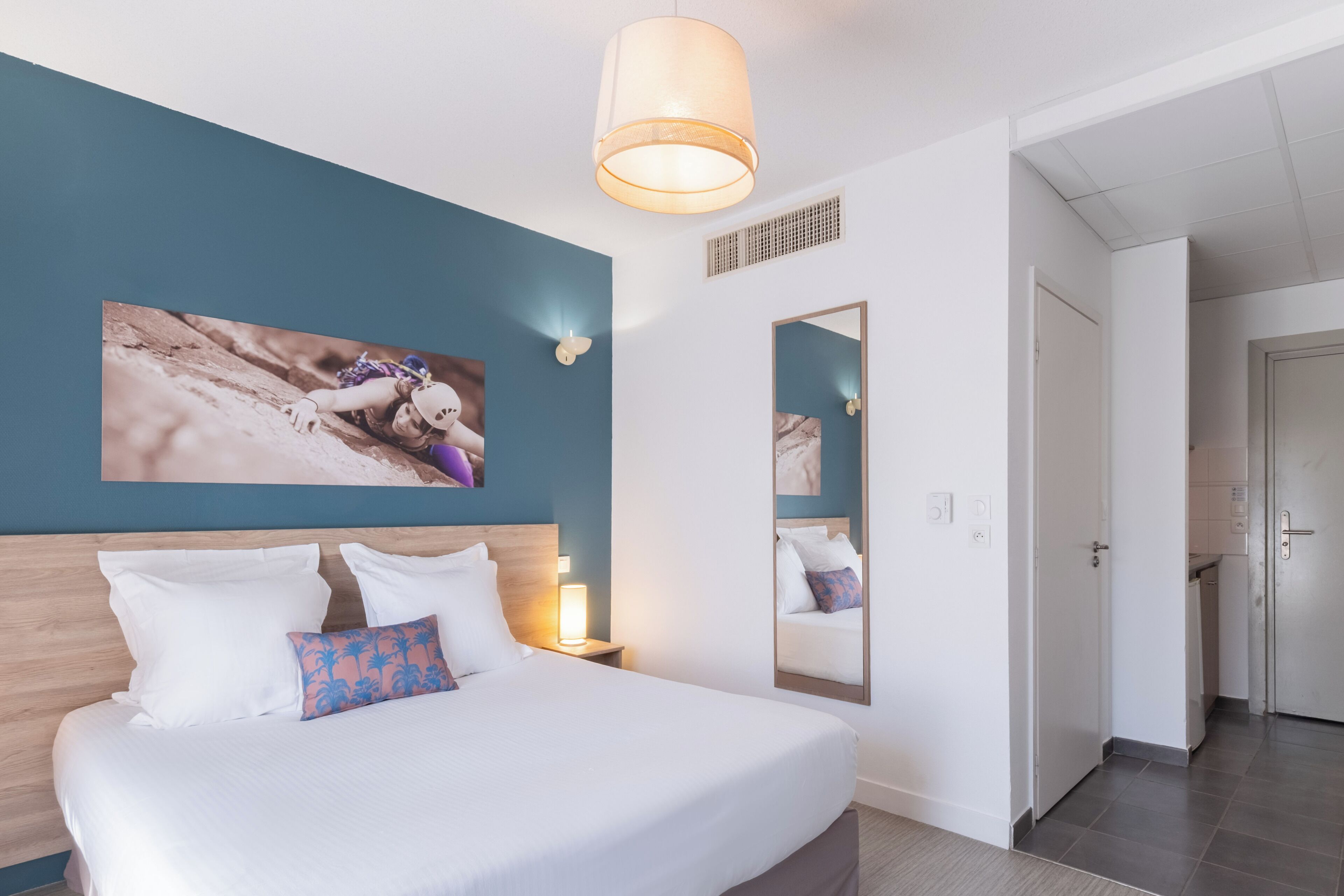 A hotel room with a large bed, a mirror, a wall-mounted picture, and a door leading to a bathroom.