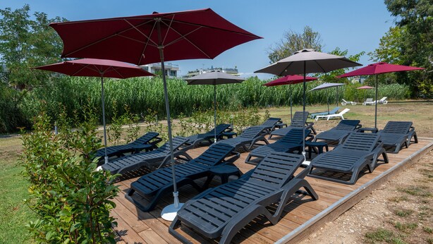 Une terrasse dotée de chaises longues et de parasols, entourée de verdure et baignée d’un ciel dégagé.