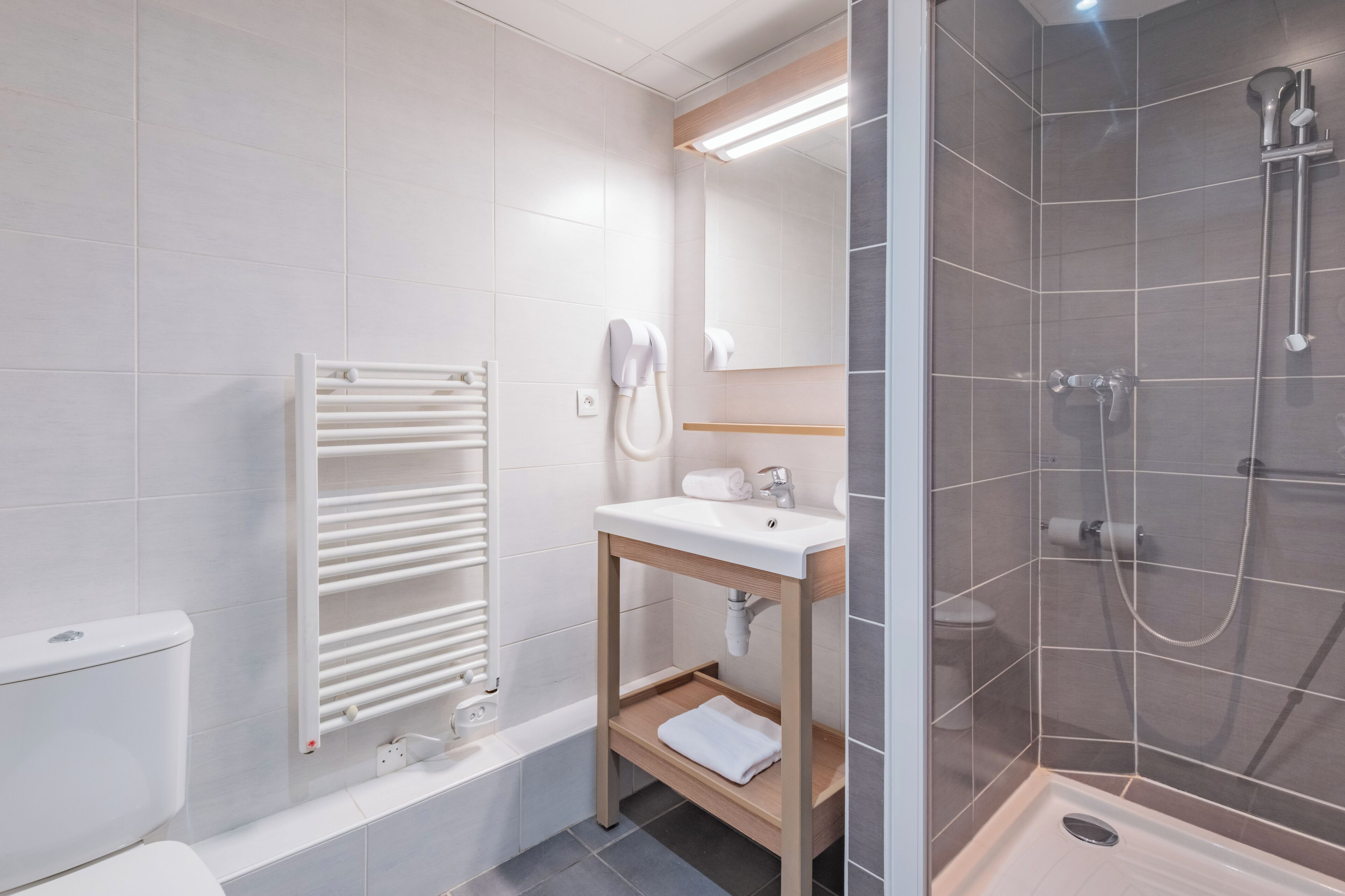 A modern bathroom with a white toilet, a towel rack, a sink with a mirror, and a glass-enclosed shower area.