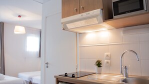Une chambre d’hôtel moderne équipée d’une kitchenette, d’un lit, d’une table de chevet et d’une plante en pot.