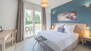 Une chambre d’hôtel comprenant un lit, un bureau, une chaise, une table de chevet avec une lampe, et donnant sur l’extérieur.