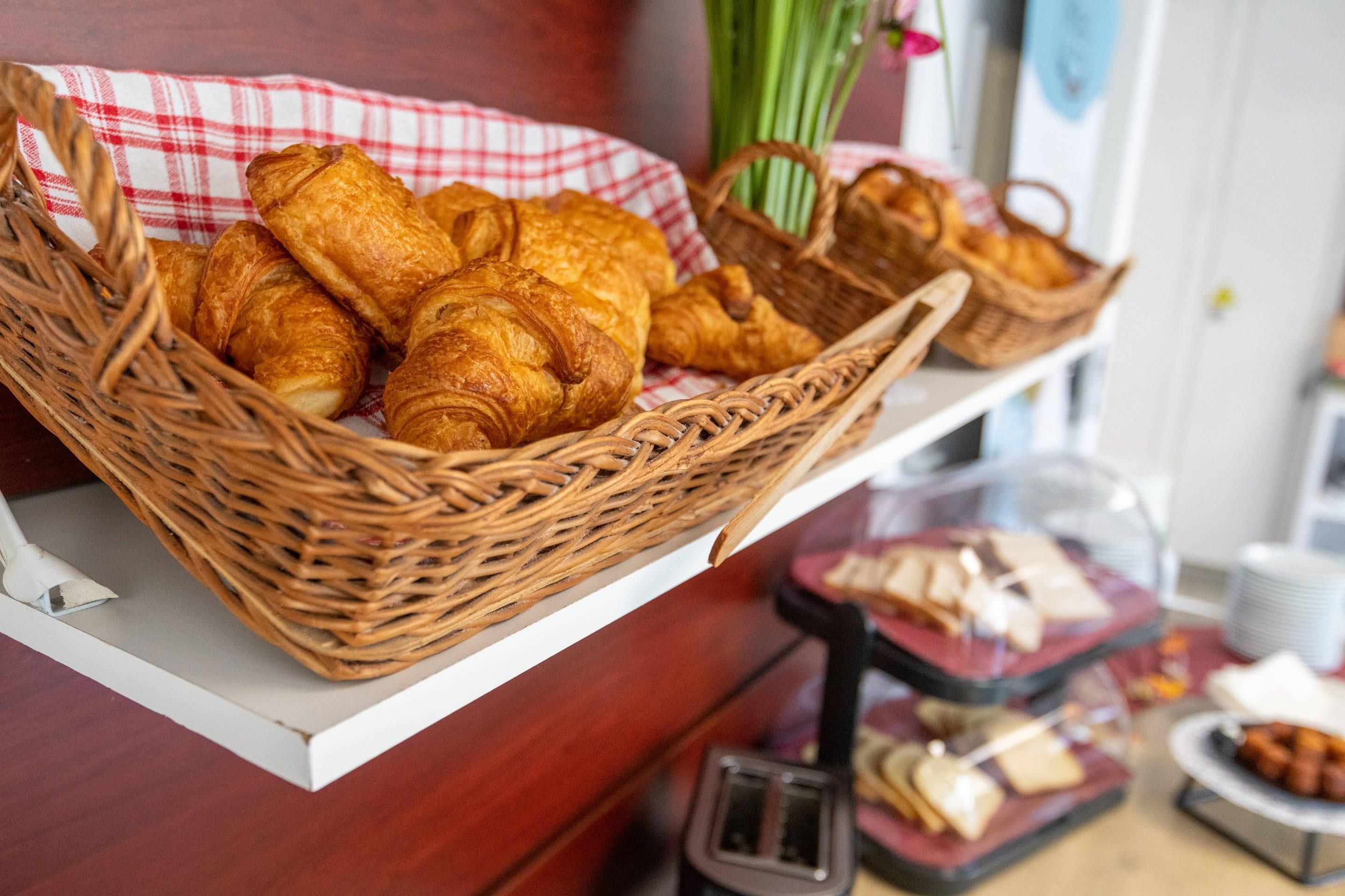 Un buffet della colazione con croissant e altri dolci in cesti di vimini, un tostapane e una selezione di formaggi e pane.