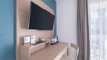 Habitación de hotel moderna con una pared de madera, un televisor de pantalla plana, un escritorio con una computadora portátil, una cafetera y una planta pequeña.