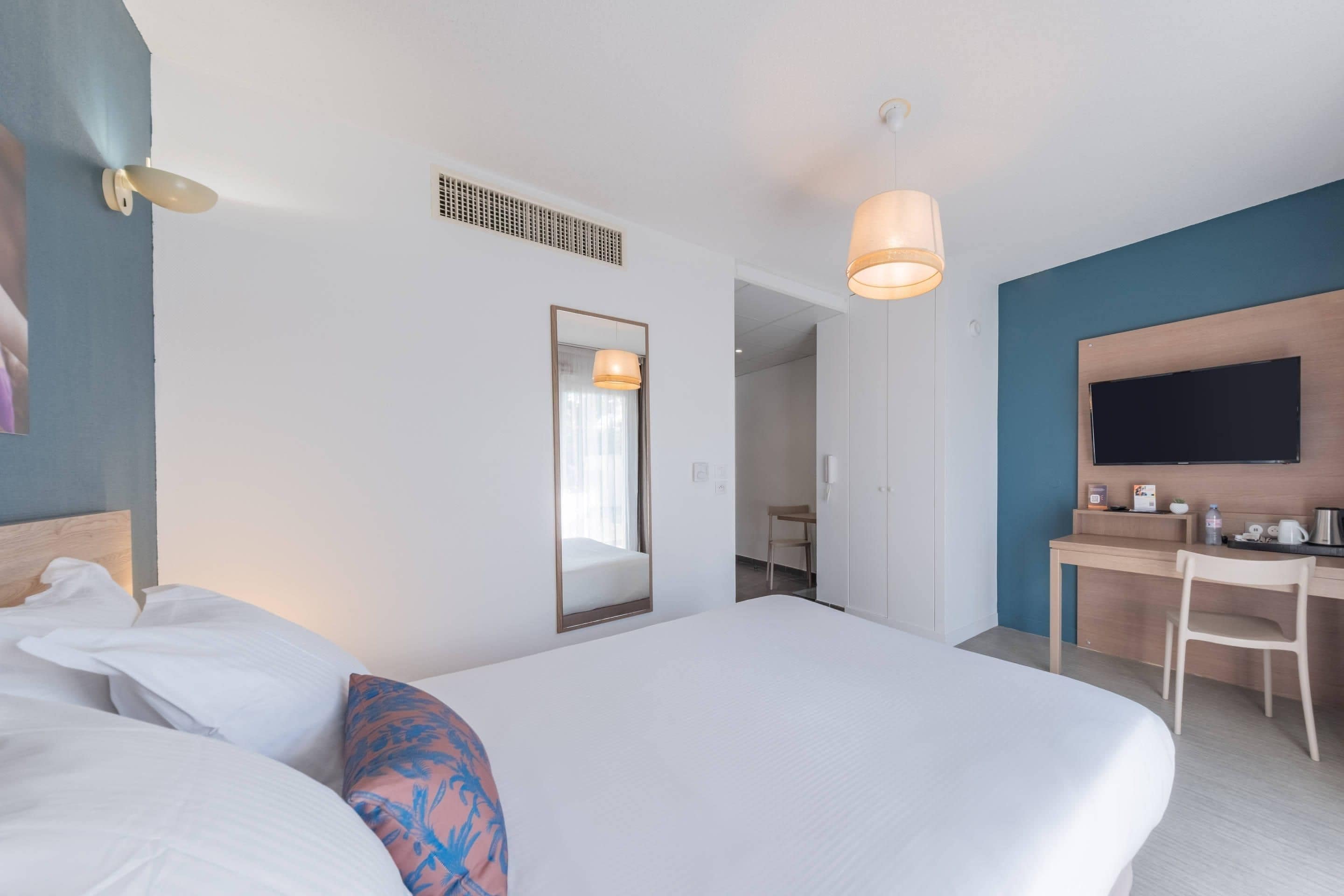 A hotel room with a bed, a desk, a chair, a television, and a mirror.