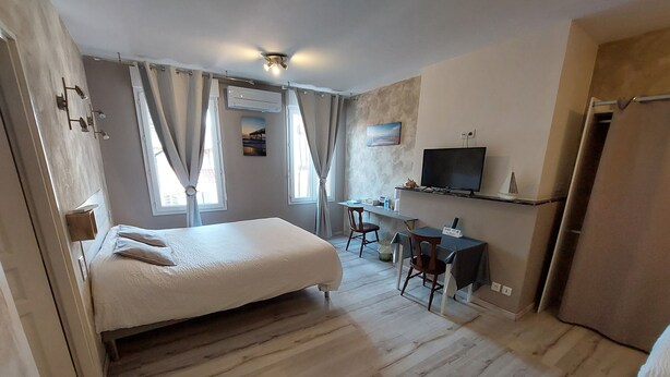 A bedroom with a bed, a desk, a chair, a television, and a window with curtains. - Hôtel Restaurant Métropole (Mirande)