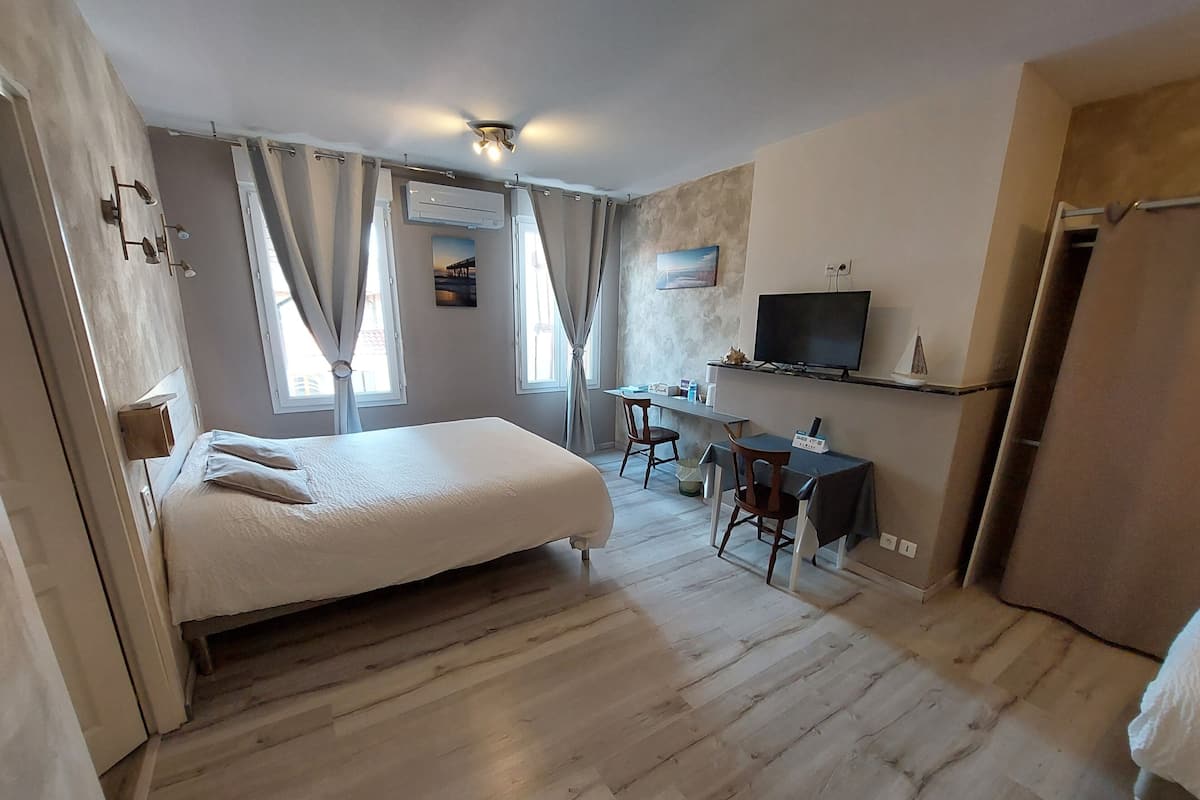 A bedroom with a bed, a desk, a chair, a television, and a window with curtains.