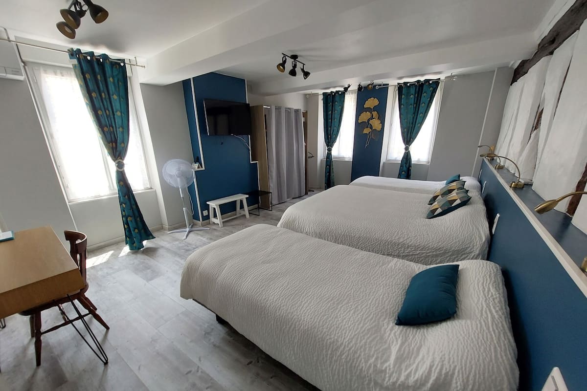A hotel room with two beds, a desk, a chair, a fan, and a TV.