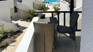 A balcony with a view of a swimming pool, white buildings, and a palm tree.