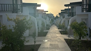 A pathway leading to a row of modern buildings with balconies, surrounded by small trees.