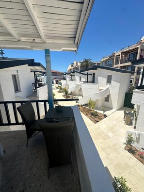 A covered outdoor area with a table and chairs, surrounded by white buildings and a clear blue sky.