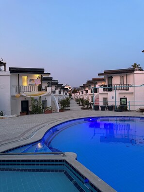 A residential area with a swimming pool, houses with balconies, and potted plants.