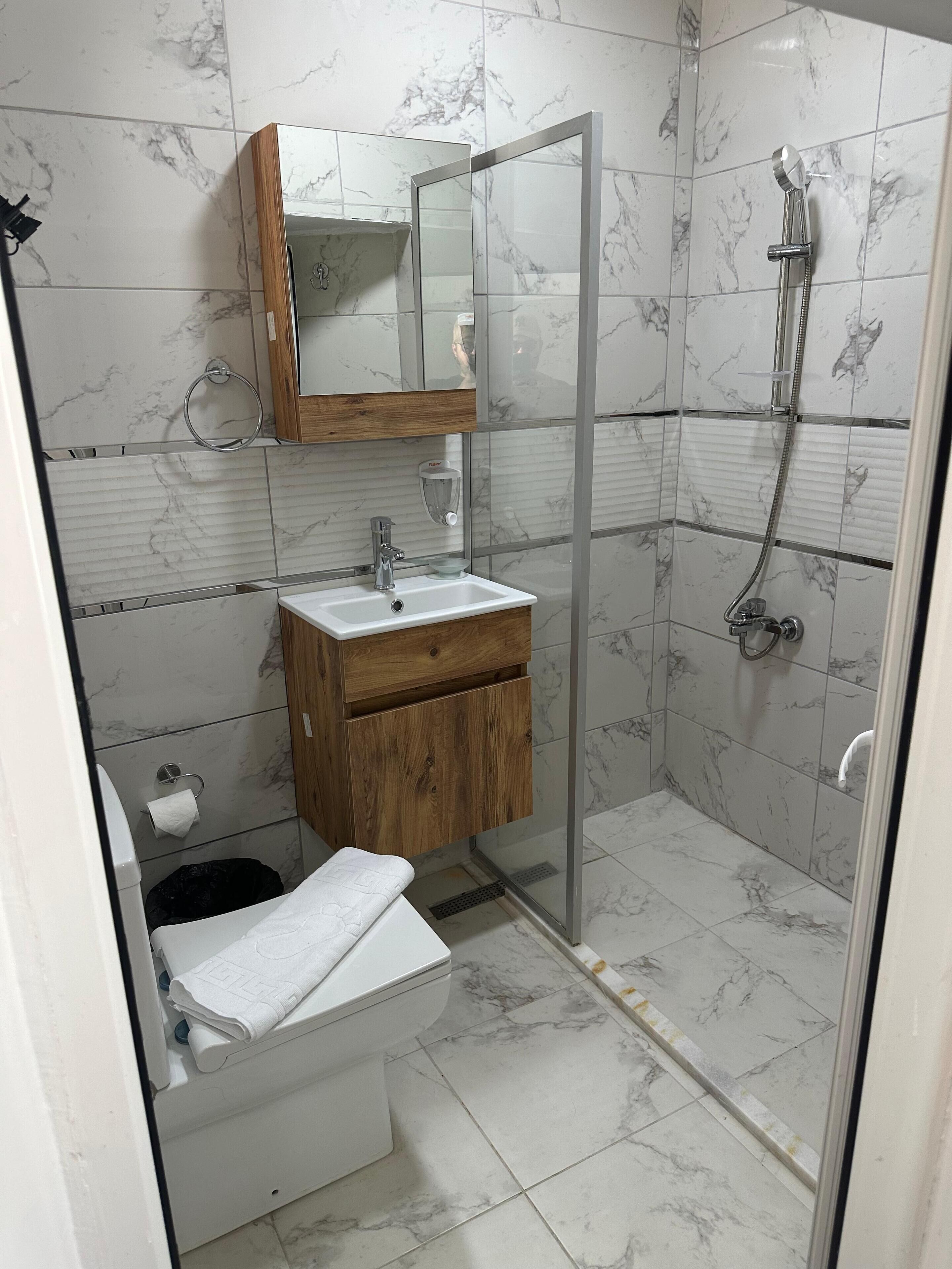 A bathroom with a marble-tiled shower, a wooden vanity with a sink, and a toilet.