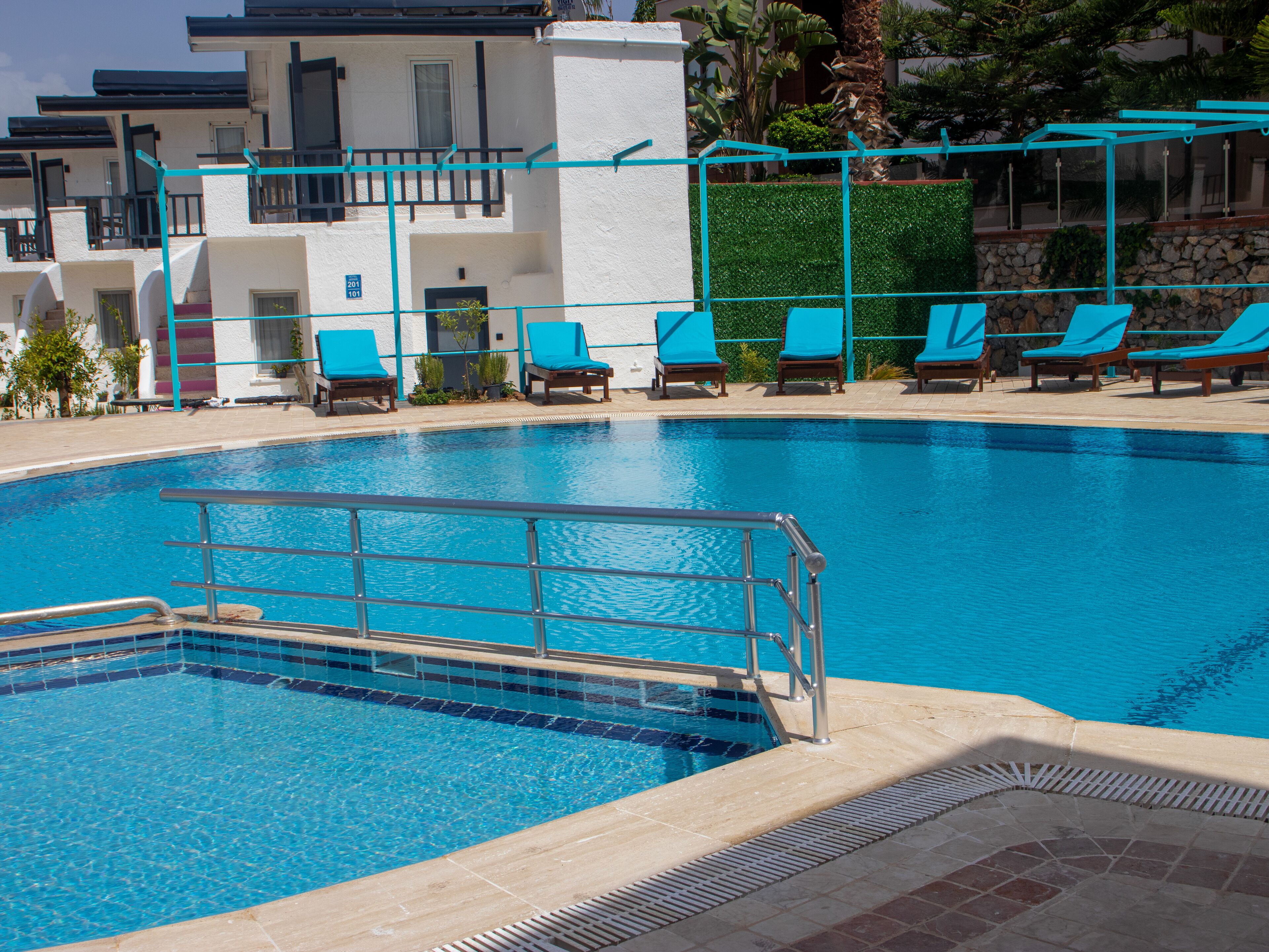 A swimming pool with a tiled edge, a metal safety railing, and several lounge chairs with blue cushions.