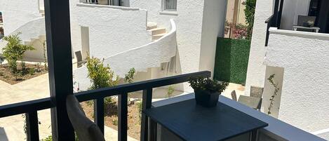 Un balcon avec une table et des chaises, donnant sur un quartier résidentiel avec des maisons et un palmier.