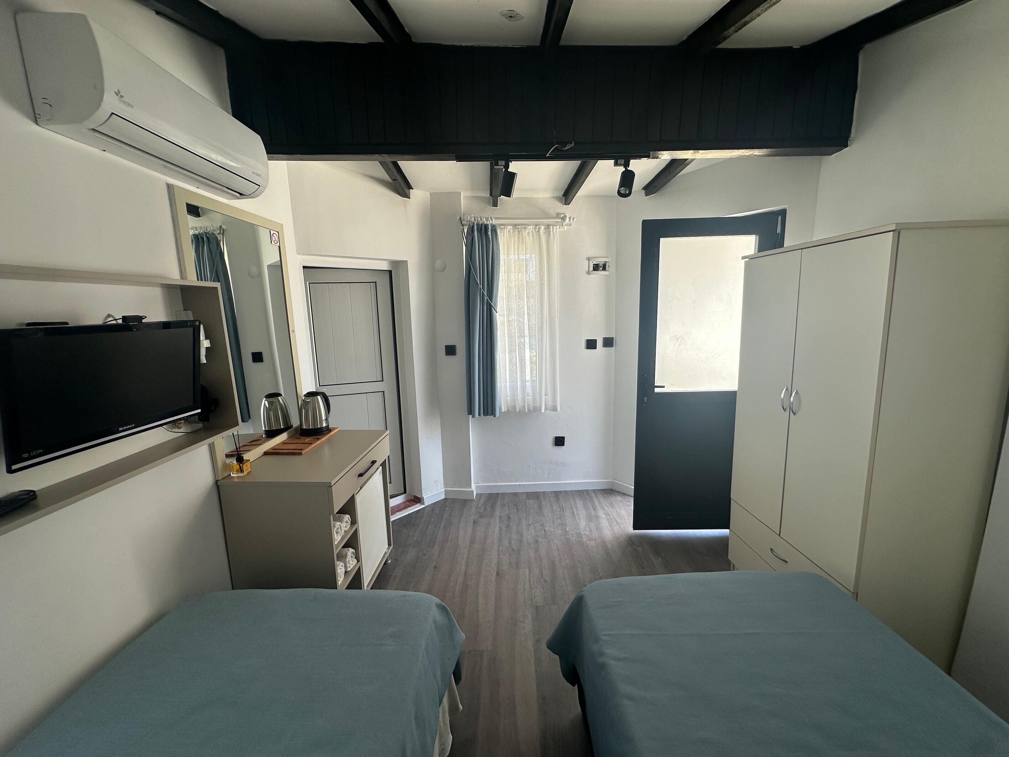 A hotel room with two beds, a TV, a desk with a kettle, a wardrobe, and a bathroom visible through an open door.