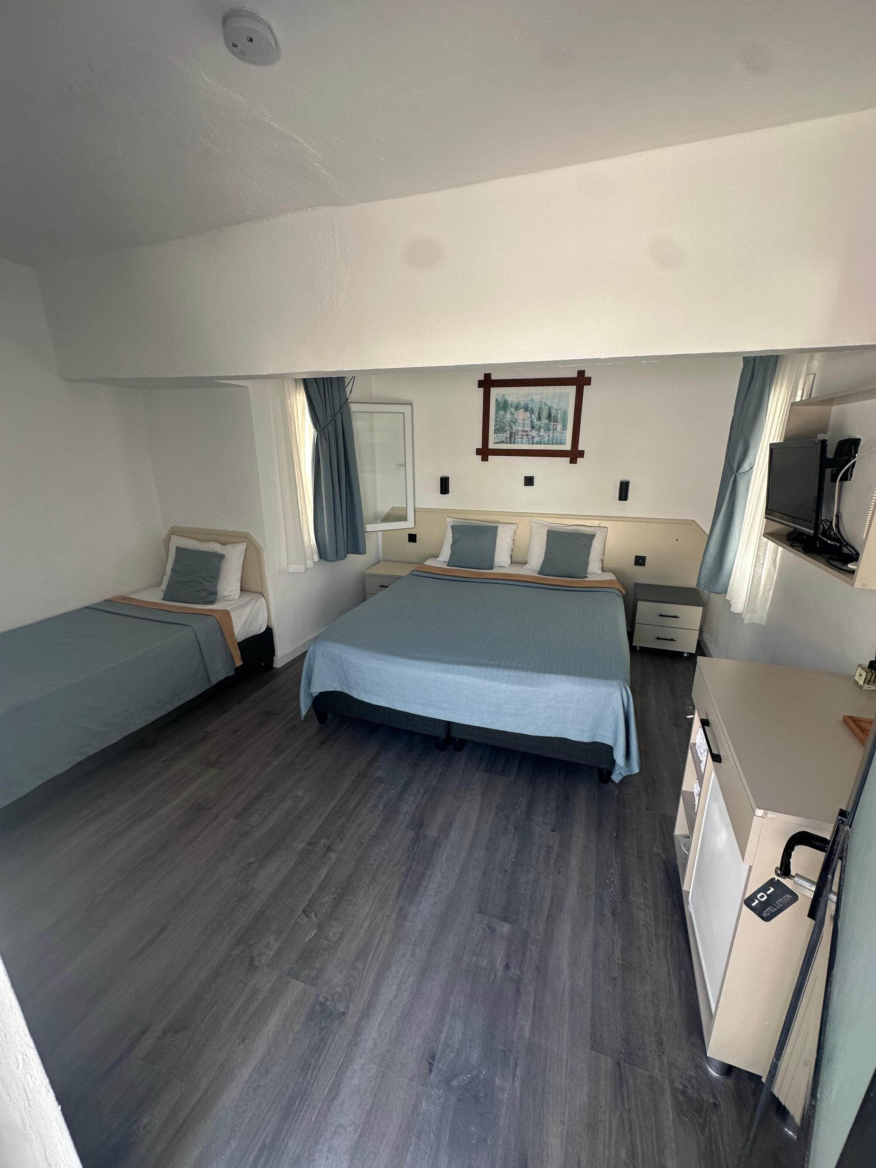 Ein Hotelzimmer mit einem großen Bett, zwei Einzelbetten, einem Schreibtisch, einem Fernseher und einer Küchenzeile.